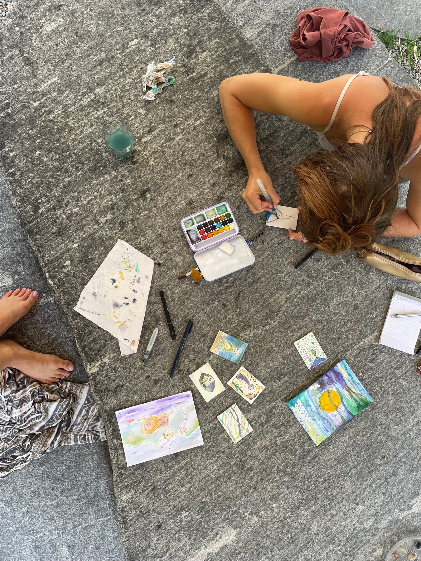 Watercolour paintings and paints spread on a stone floor while someone paints
